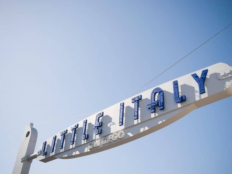 White and blue sign that reads "Little Italy San Diego" against the blue sky with sun