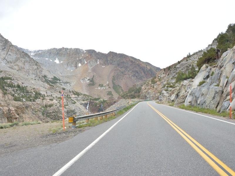 the two-lane highway 120 tioga road with mountains with some remaining snow pockets remaining in the crevices