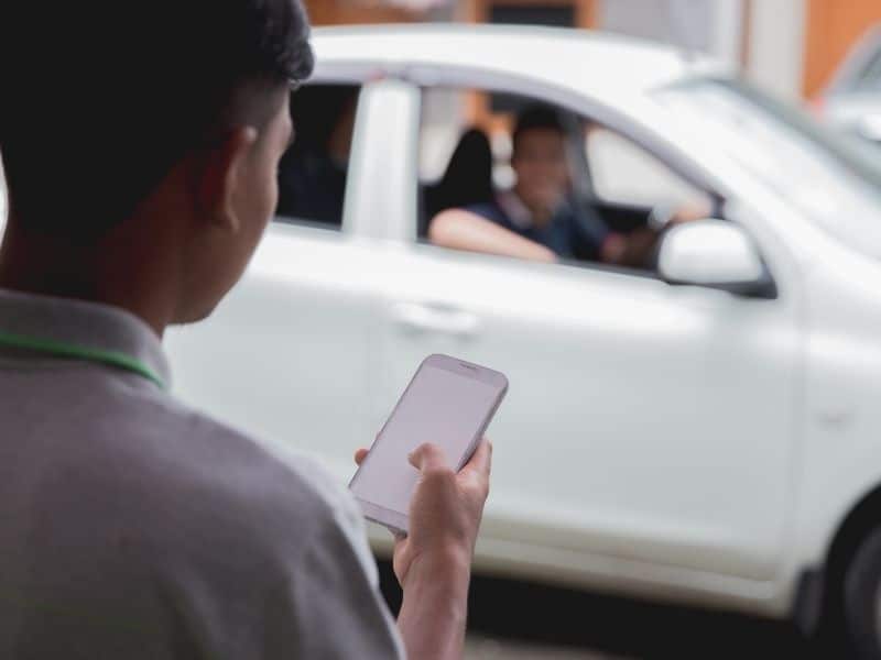 man holding a phone looking at his uber app while his driver is arriving