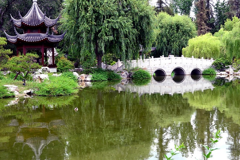 white bridge reflected into a pond and a two-tiered pagoda also reflected in a green chinese-inspired pond