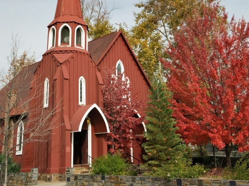 a red church next to a christmas tree and a red maple tree in sonora california