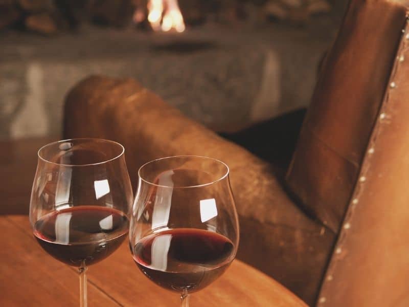 two glasses of cabernet sauvignon red wine on a table next to a leather armchair with a fire in the background in napa in winter