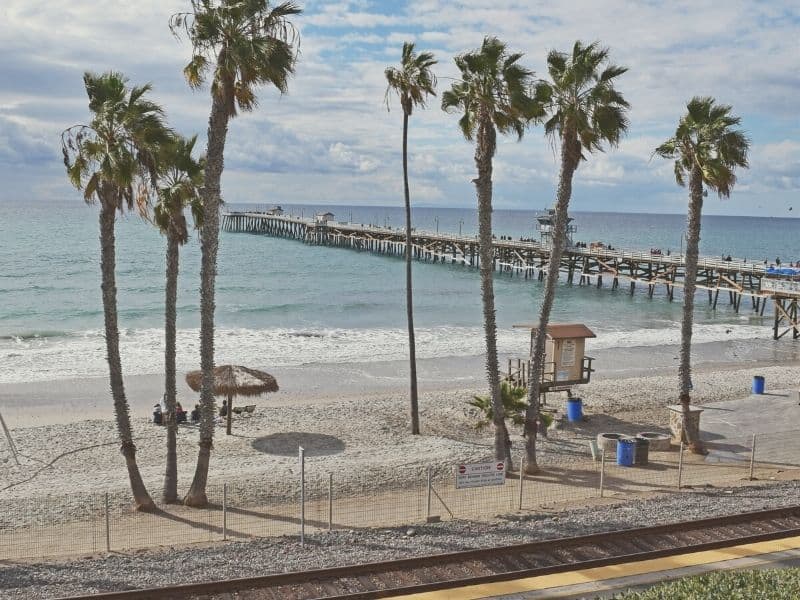 train tracks in front of the beach and long wooden pier in southern California with palm trees