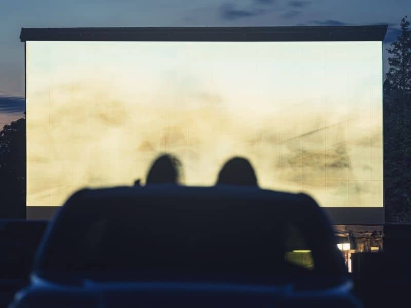 a drive in movie theater screen and two heads watching the screen