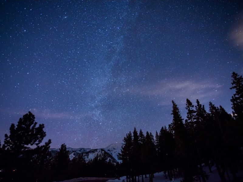 the snow-peaked mountains in the distance with trees and a little bit of the milky way visible while stargazing in lake tahoe california