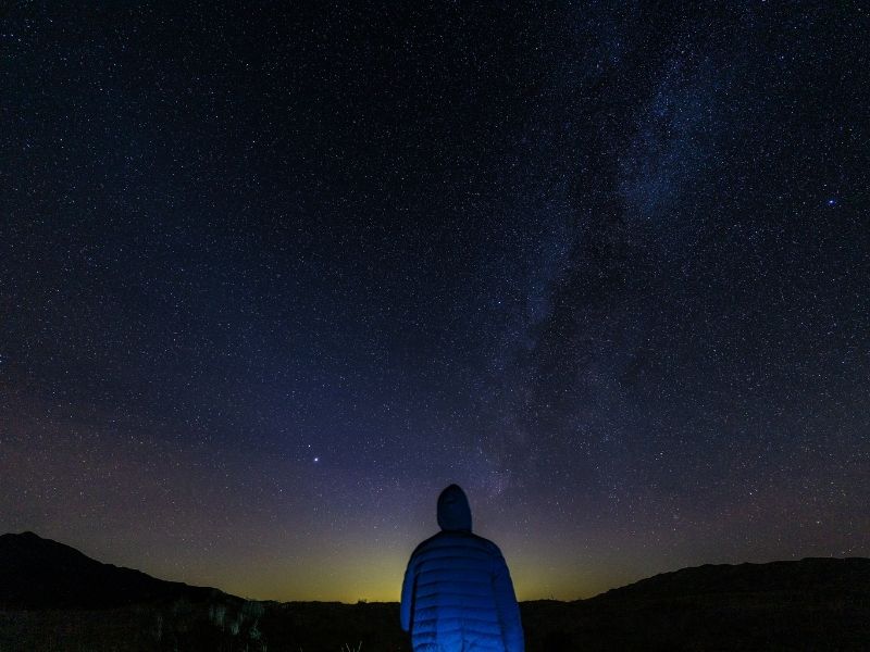 man wearing jacket with hoodie looking towards the night sky