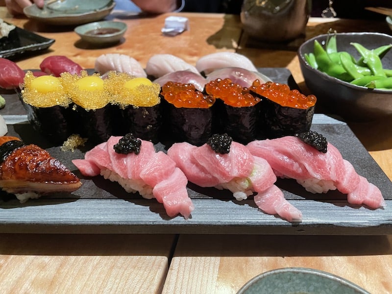 delicious toro sushi and ikura sushi on a plate and edamame behind it