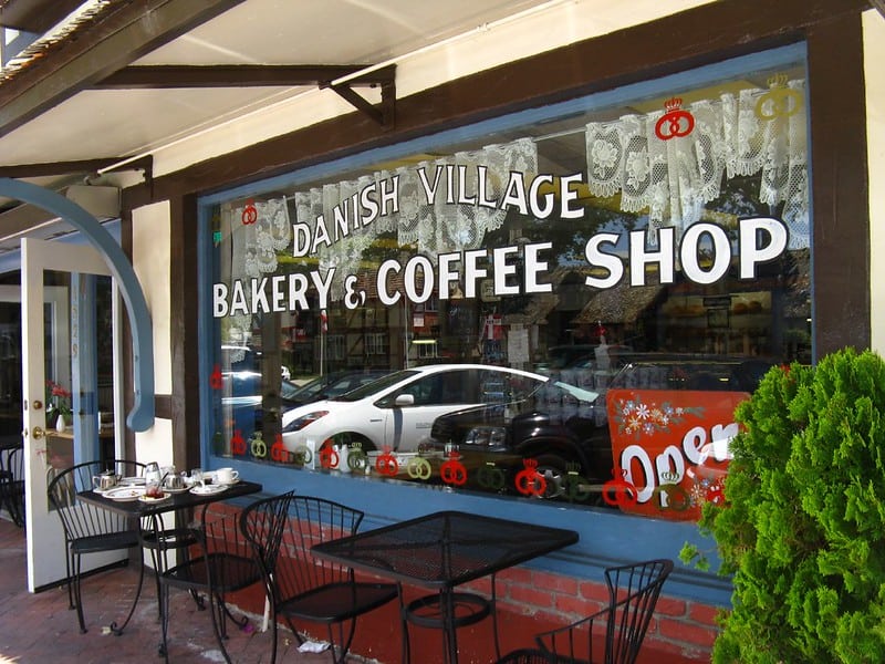 window in solvang that says 'danish village bakery and coffee shop' with tables in front