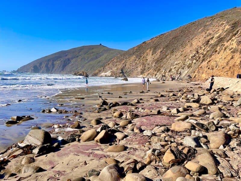 view of pfeiffer beach in the middle of the day with people walking on the purple sand beach