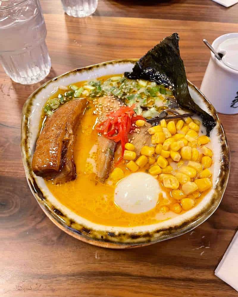 Bowl of ramen with soft boiled egg, corn, seaweed, and two different types of pork.