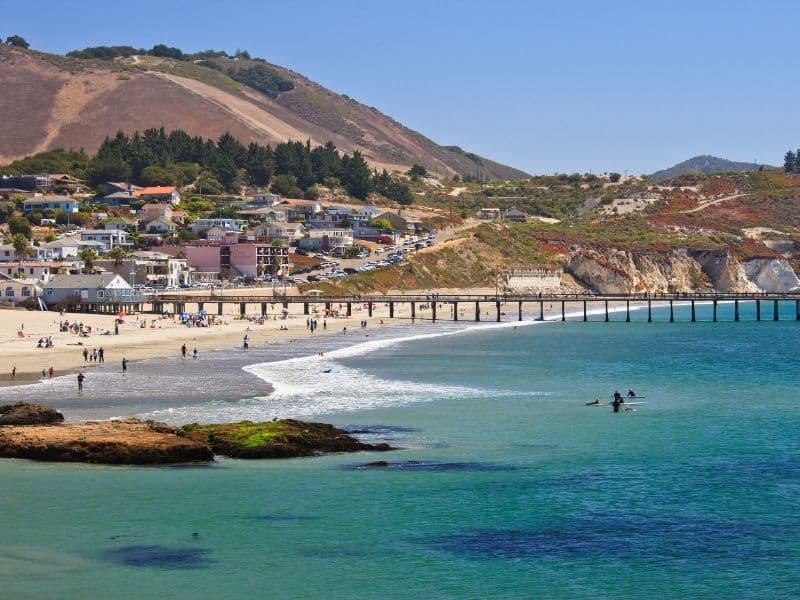 the blue water at avila beach with a pier and mountain in the distance and cityscape