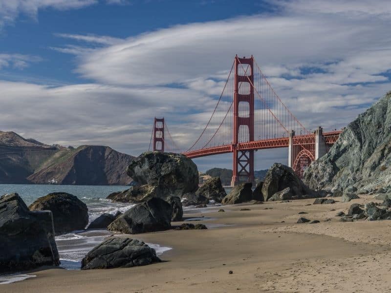 sandy beach with large rocks on the beach and a view of the red golden gate bridge