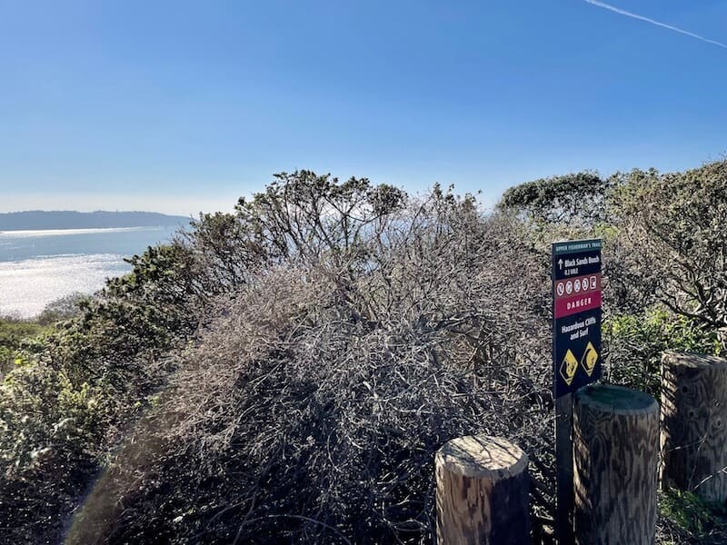 black sands beach trailhead with brush and pacific ocean in distance