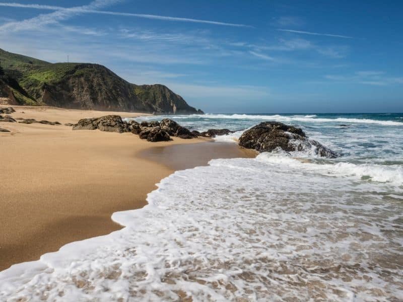 surf coming up onto the sandy shores of gray whale cove state beach with hills in the background