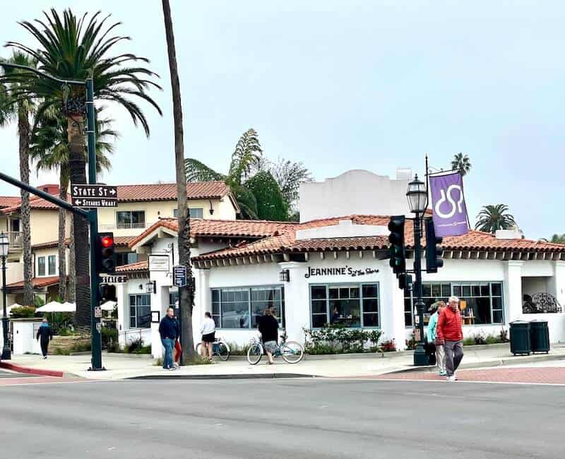 a man crossing the street on state street in front of jeannine's on a foggy day in santa barbara with palm trees in the distance