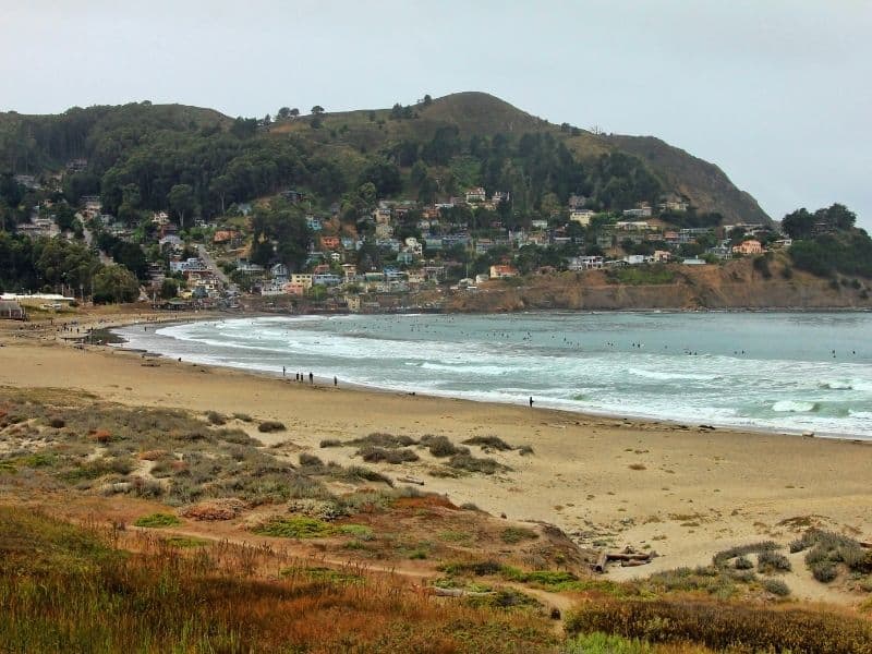 the beach at pacifica on a foggy day with people walking along the water's edge and houses on the beach in the distance