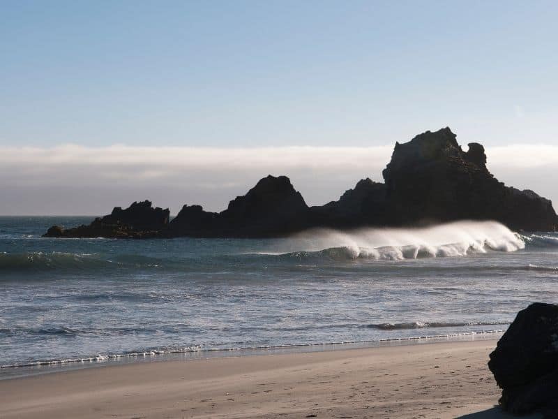 big waves coming into the purple sand beach of big sure with rock formations nearby