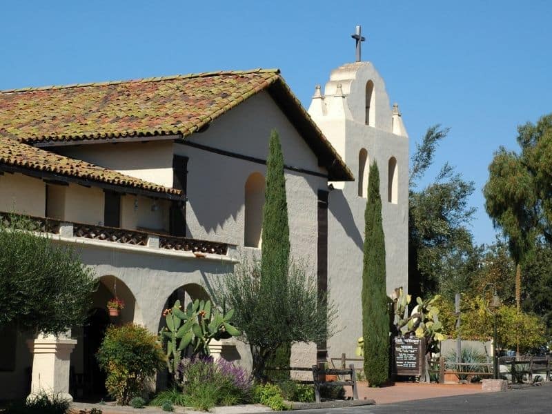 photo of a historic mission with trees and cacti in front in Spanish architectural style