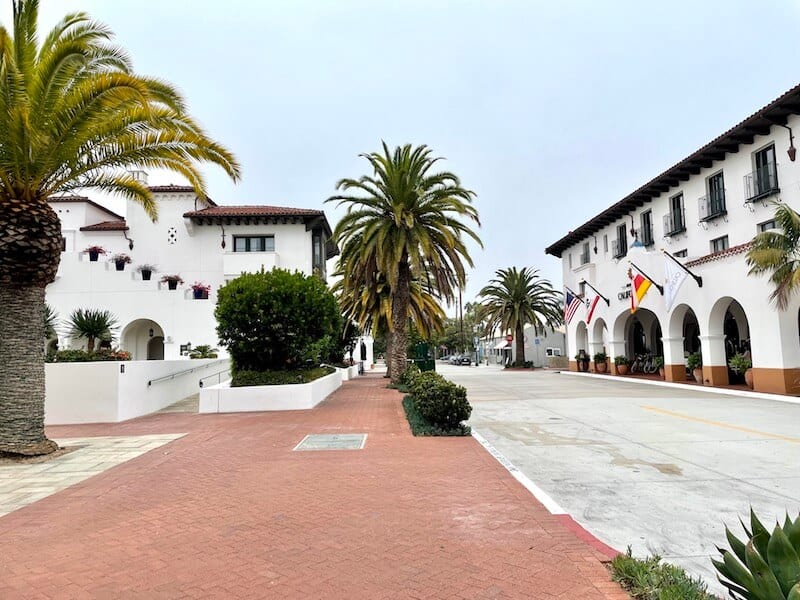 palm trees and white spanish colonial revival style architecture with archeways and red tile and flags outside of one of the buildings.