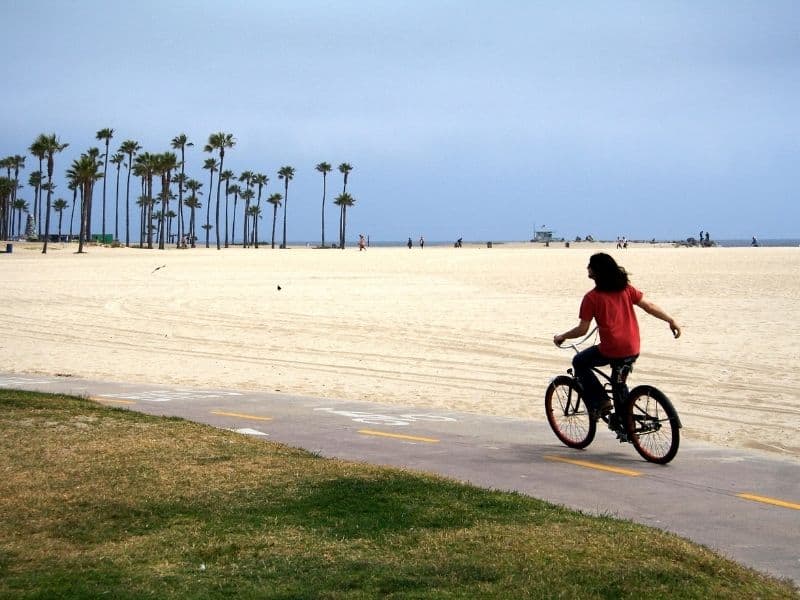 man with long hair riding a bicycle on the venice beach bike path