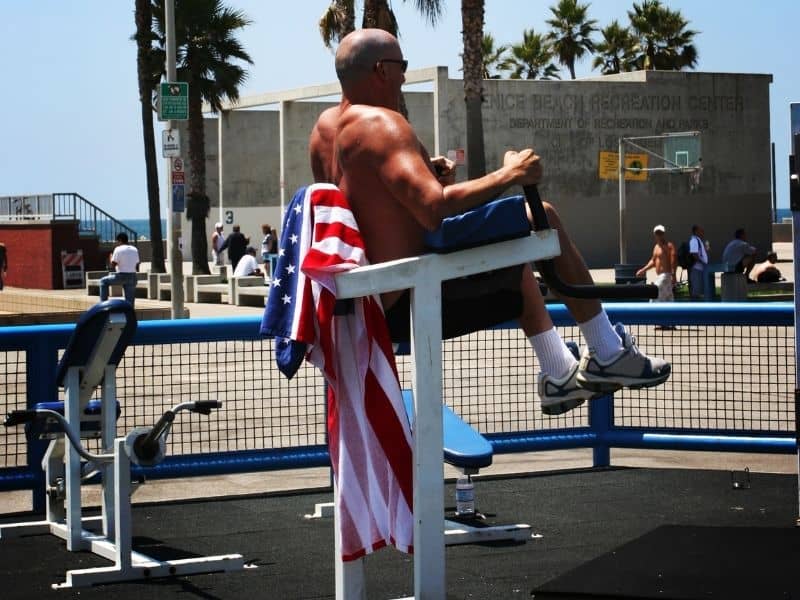 man with american flag towel working on at an outdoor gym in venice beach california