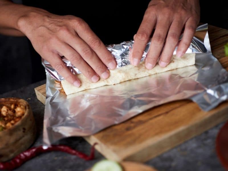 hands rolling a burrito in tin foil