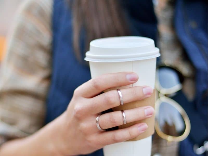 coffee in someone's hand wearing three rings and a vest and sunglasses