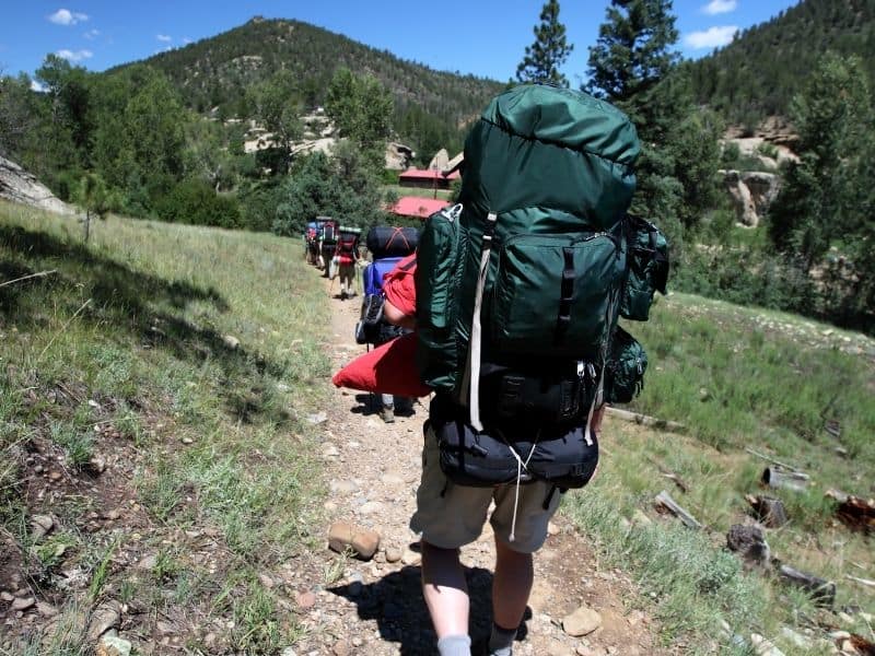 A row of people walking in the mountains carrying large backpacks