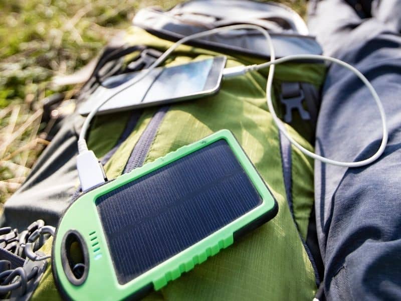 a solar phone charger and a person charging their phone in the grass