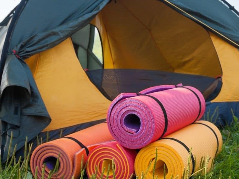 four different foam sleeping pads on the ground near a yellow tent