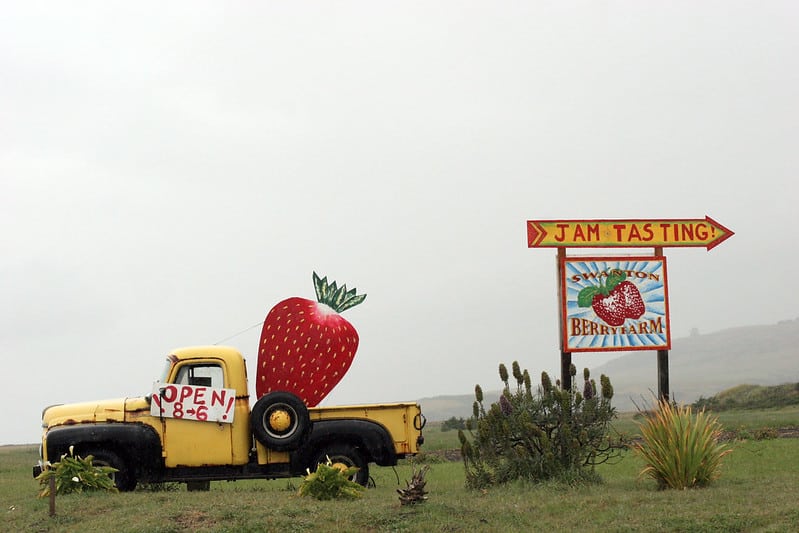 yellow truck with cardboard strawberry and sign saying "jam tasting" and "strawberry farm" and "open 8 to 6"